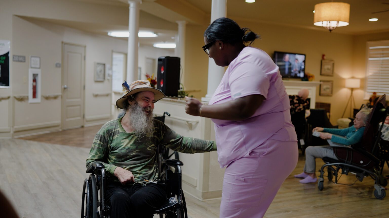 A nurse smiles and talks to a resident of a skilled nursing facility in a lobby area