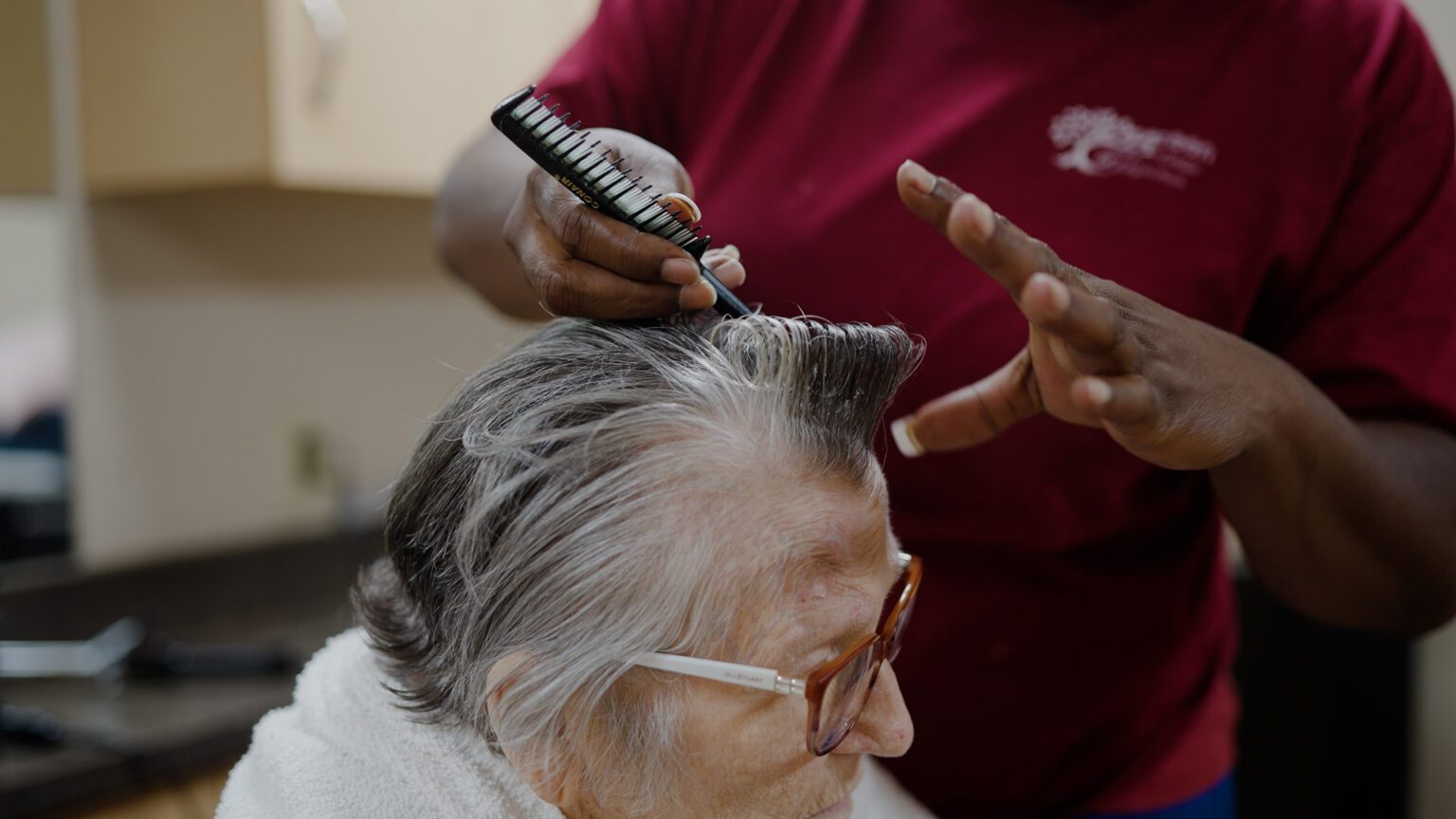 A woman is getting her hair done by a stylist at a skilled nursing facility